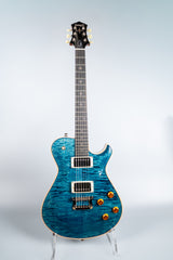 Blue Knaggs Kenai electric guitar on a stand against a light gray background