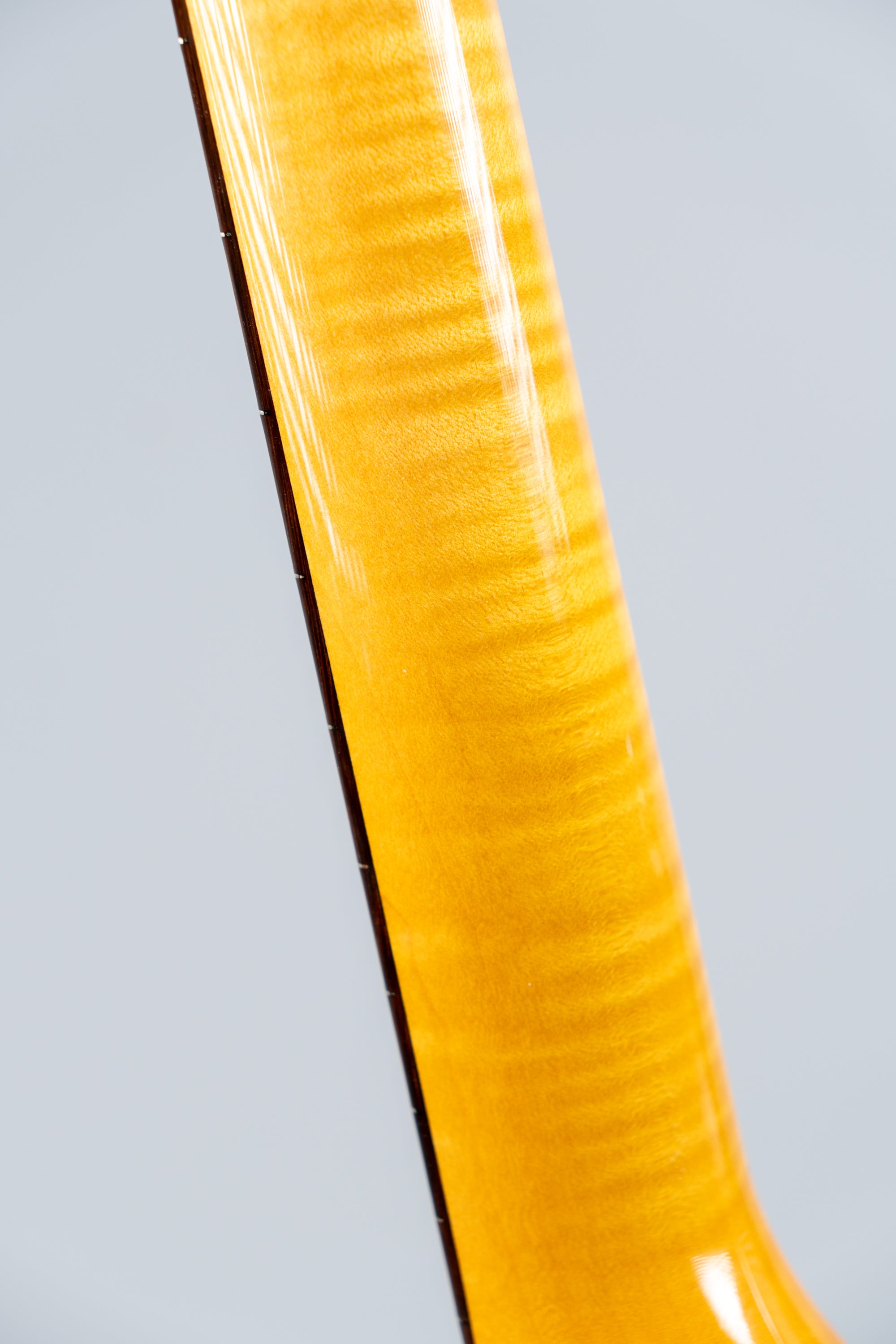 Close-up of a Knaggs Severn electric guitar flamed maple neck on a gray background