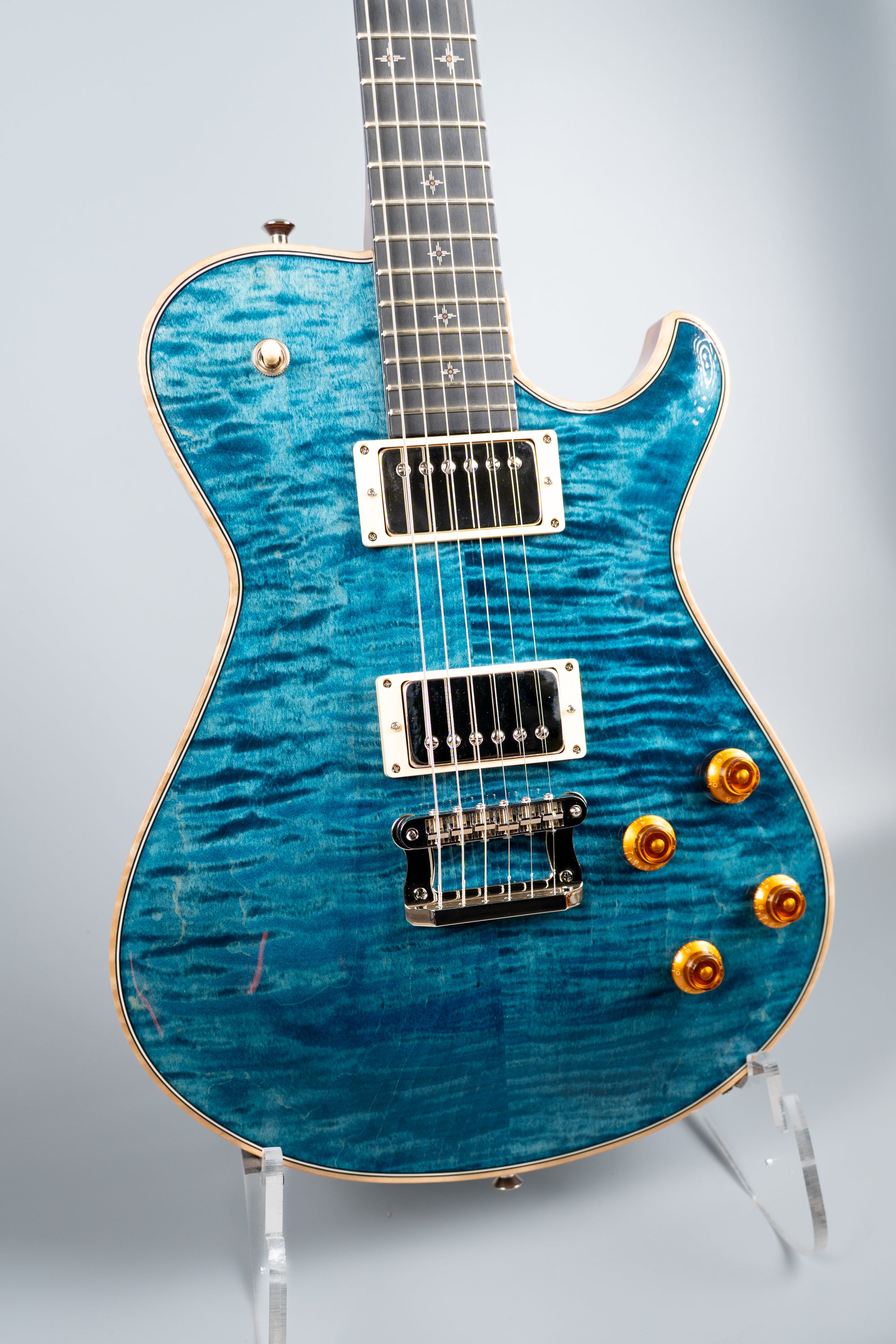 Blue Knaggs Kenai electric guitar on a stand against a light gray background