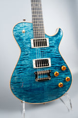 Blue Knaggs Kenai electric guitar on a stand against a light gray background