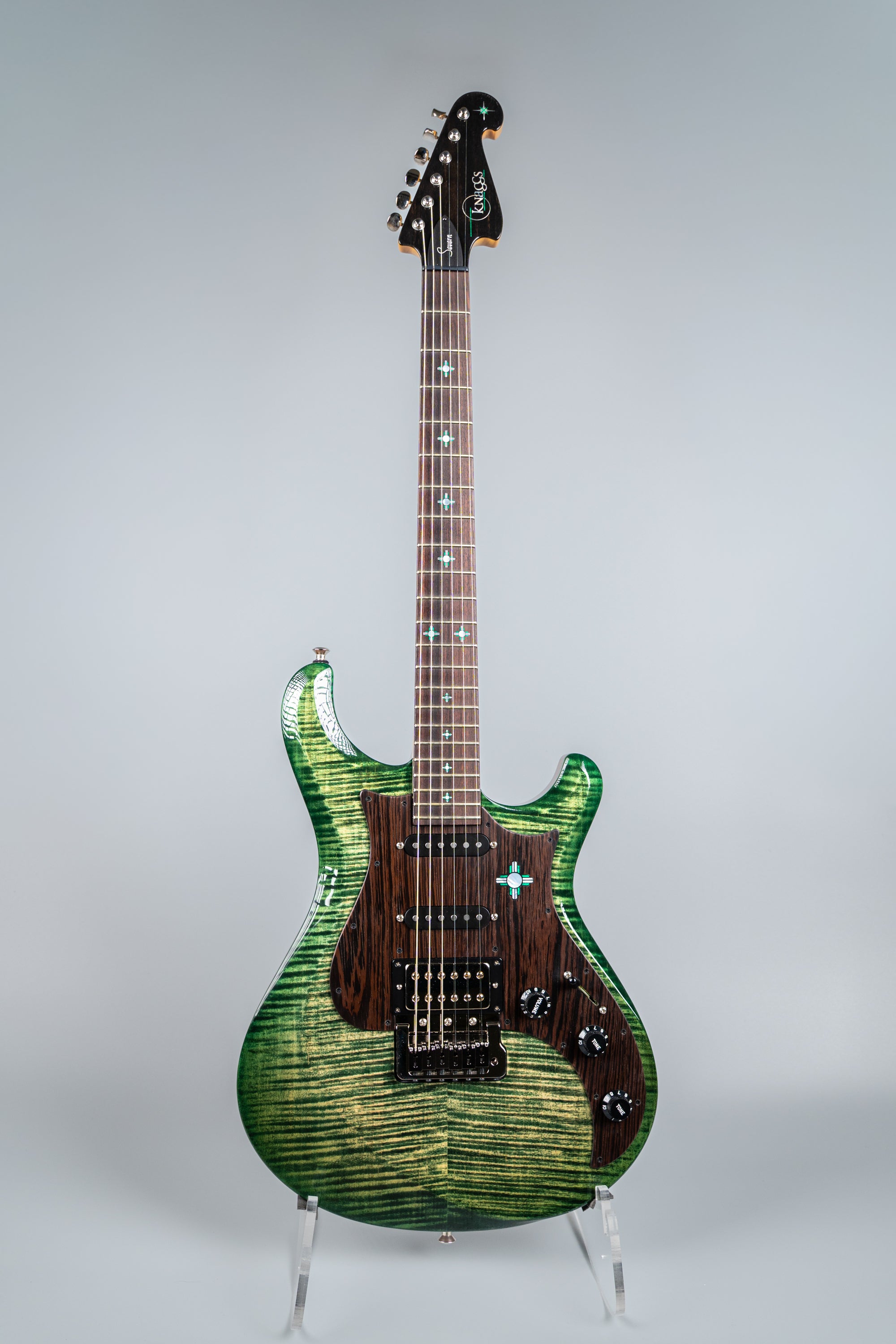 Green electric guitar Knaggs Severn on a stand against a gray background